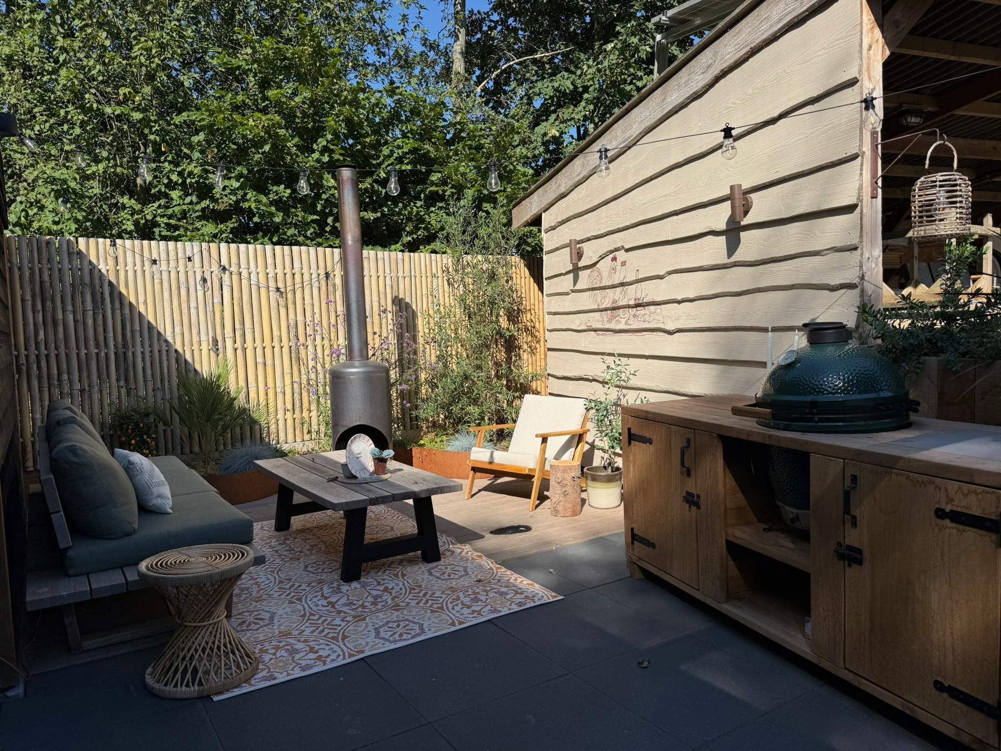 Tuininspiratie terras met loungeset en vloerkleed bij overkapping met bamboeschutting en buitenkeuken