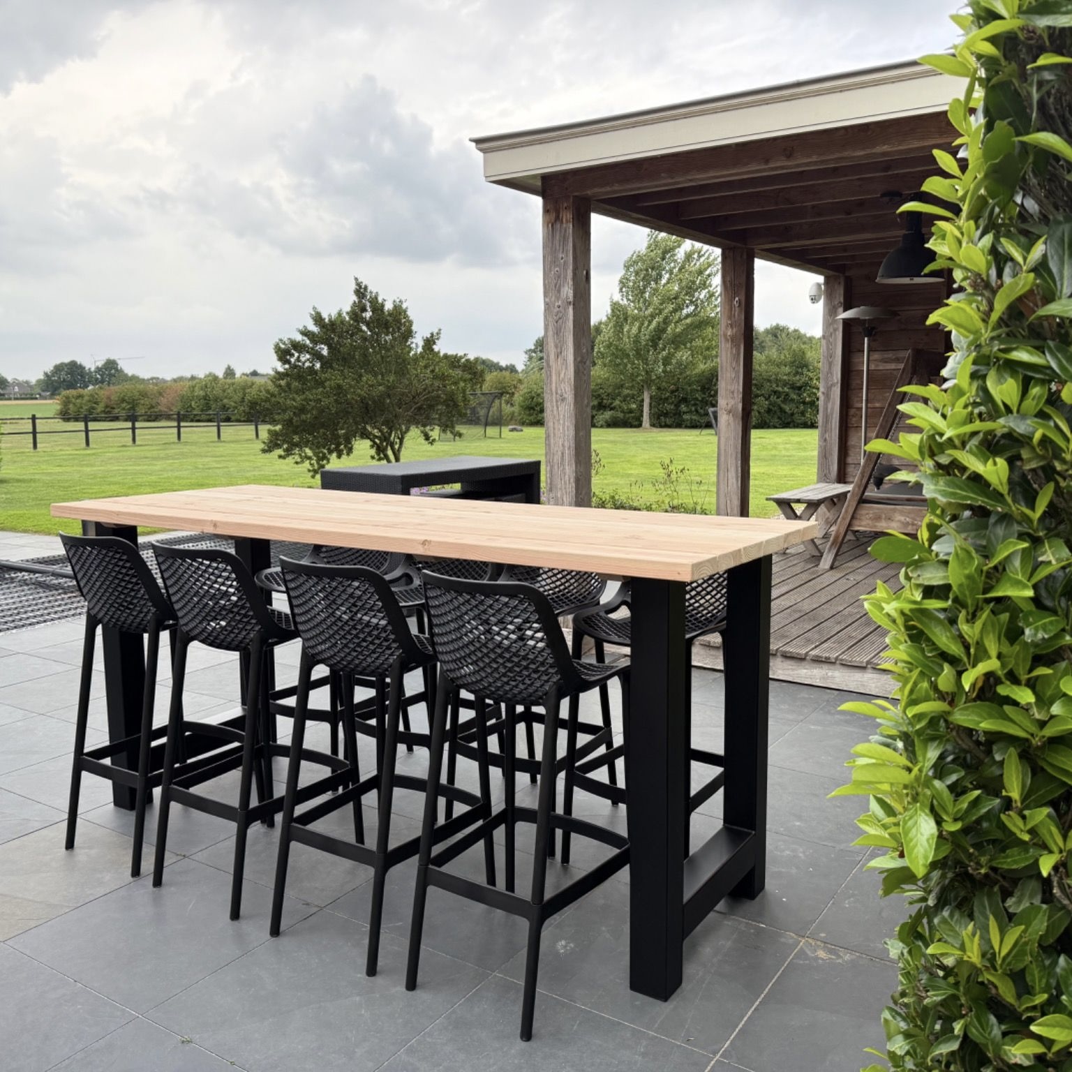 Barkruk zwart bij een bartafel op het terras in een groene tuin