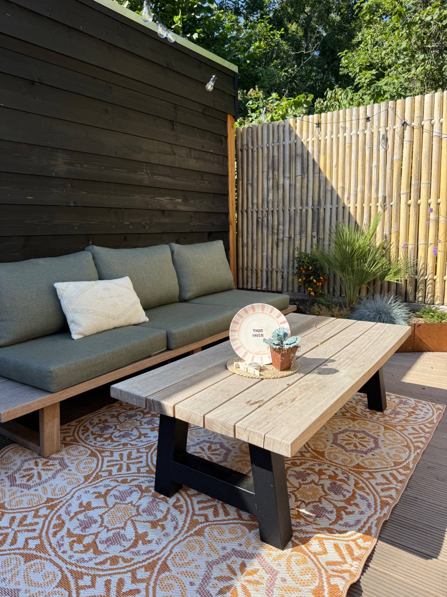 Tuininspiratie terras met loungeset en vloerkleed bij overkapping met bamboeschutting en buitenkachel
